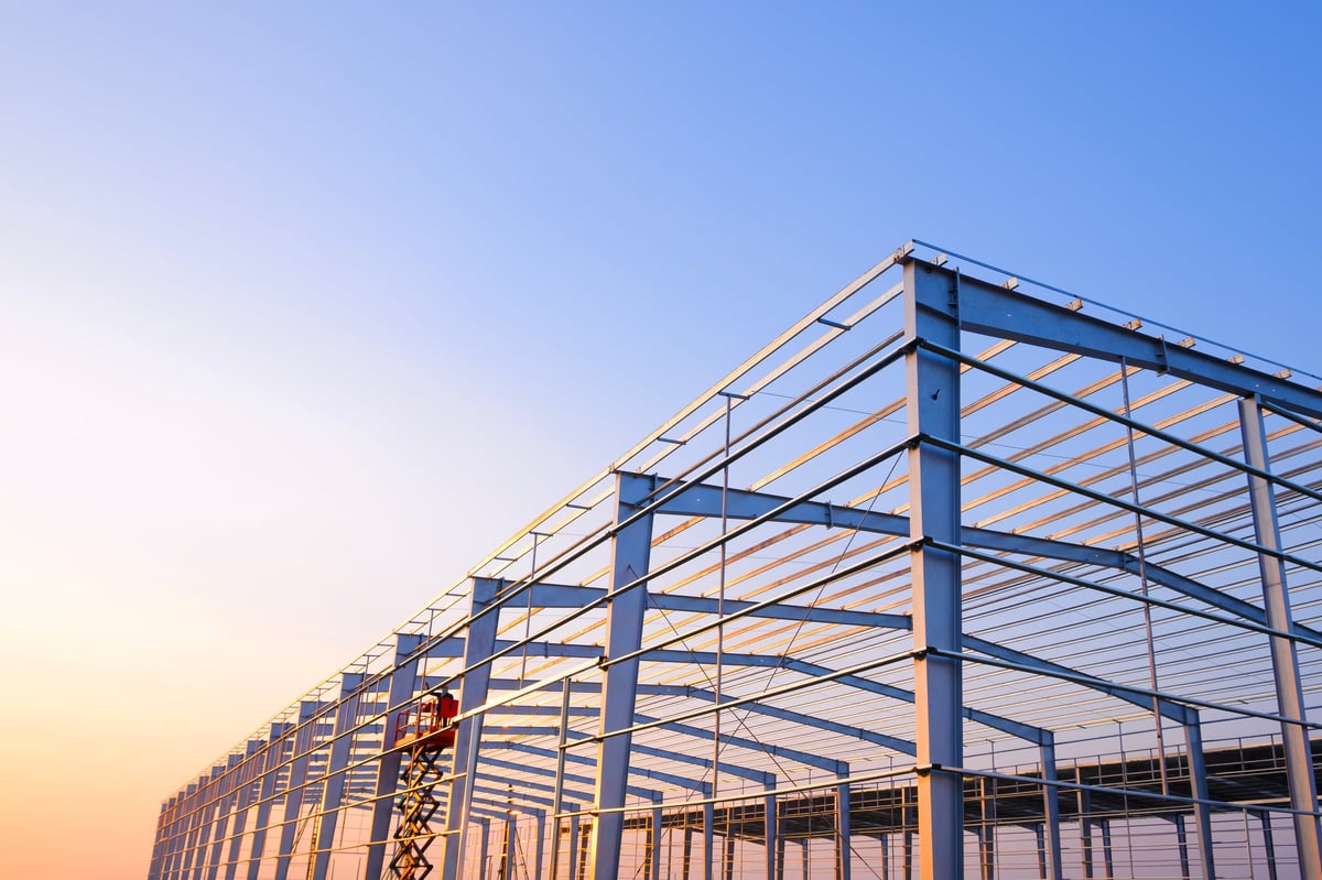 Metal posts and roof beam structure of factory industrial building framework in construction site against sunset sky background