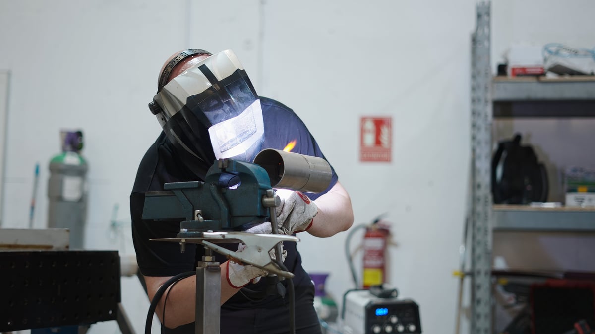 Experienced welder performing precise tig welding, joining metal pipes inside industrial workshop setting with professional metalworking techniques