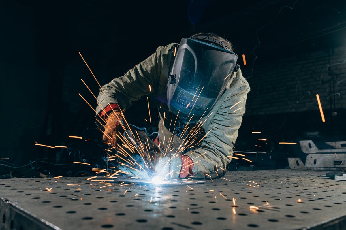 A welder works on metal, creating bright sparks while wearing protective gear.